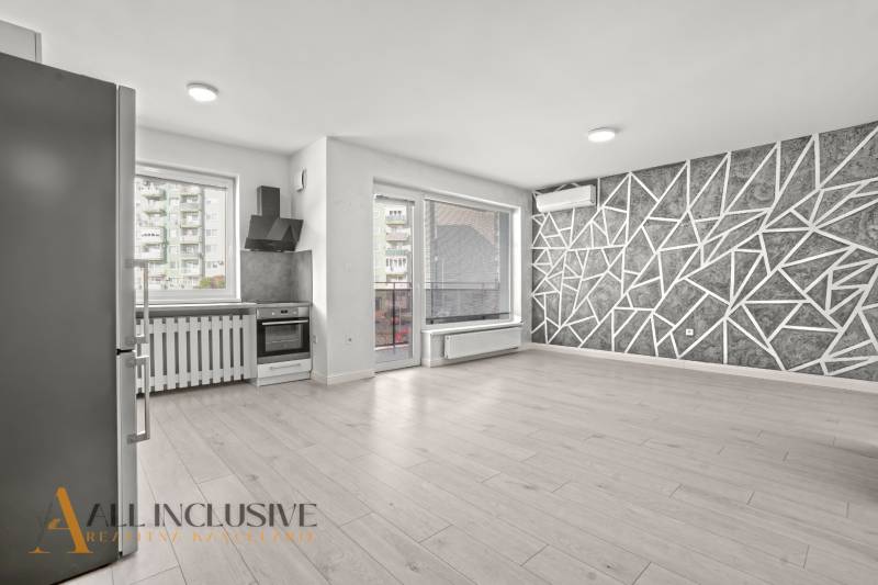 Küche und Wohnzimmer in einer Zweizimmerwohnung mit Holzboden und geometrischer Wand.