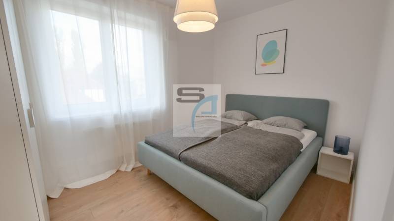 Schlafzimmer mit großem Bett, Vorhängen und Holzboden in einer Zweizimmerwohnung.