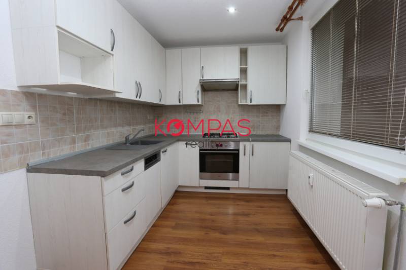 Küche in einer 3-Zimmer-Wohnung mit weißen Schränken und einem Boden in Holzoptik.