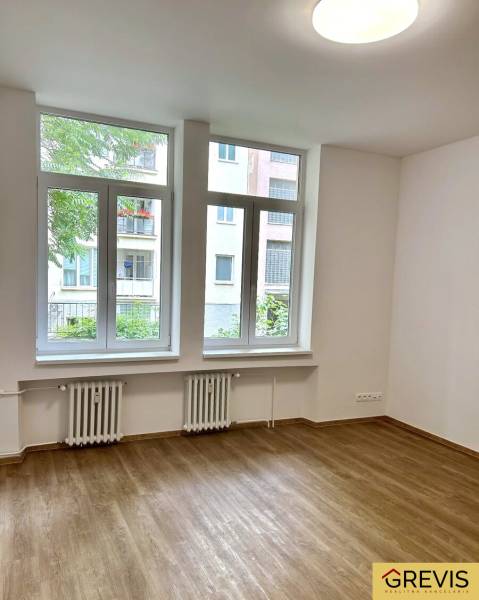 Ein Zimmer in einer 4-Zimmer-Wohnung mit großen Fenstern und einem Boden in Holzoptik.