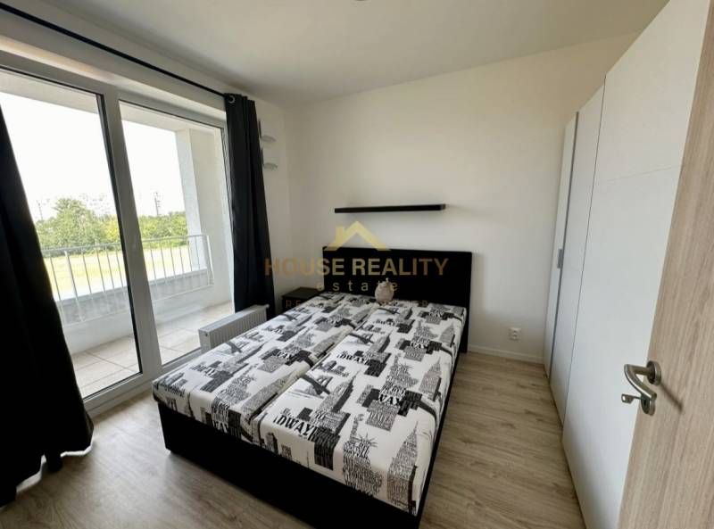 Schlafzimmer in einer 2-Zimmer-Wohnung mit Bett, Schrank und Balkon mit Holzboden.