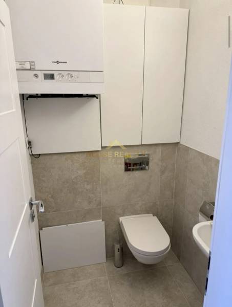 Toilette in einer 3-Zimmer-Wohnung mit einem modernen Wandkessel und beigefarbenen Fliesen.