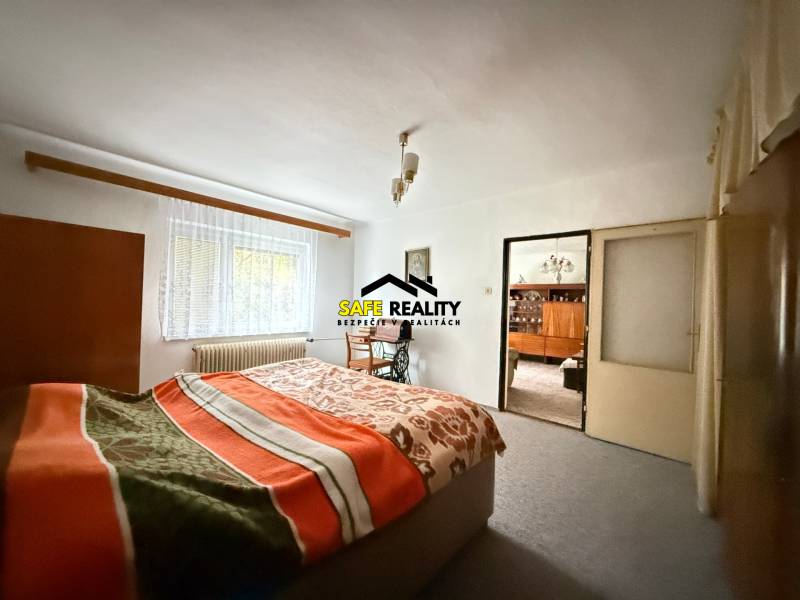 Schlafzimmer im Einfamilienhaus mit hellem Teppich, Fenster und Bett mit Decke.