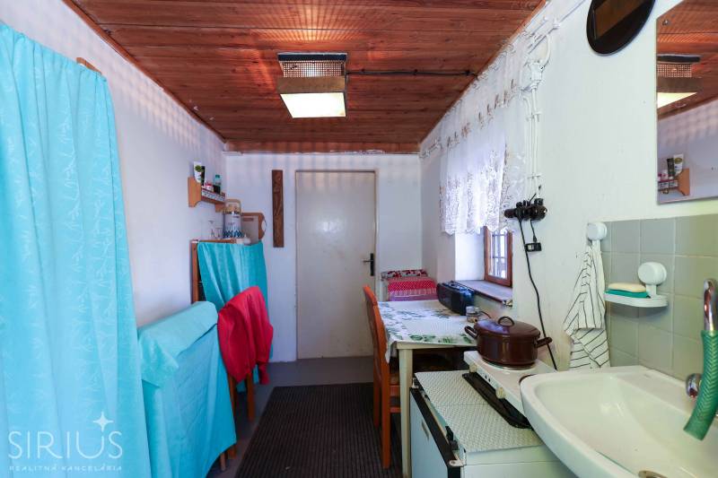 Küchenecke in den Gärten mit Vorhängen, Holzdecke und einfacher Ausstattung.