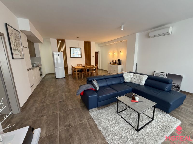 Wohnzimmer mit blauem Sofa und Küche in einer Zweizimmerwohnung, Boden mit Holzdekor.
