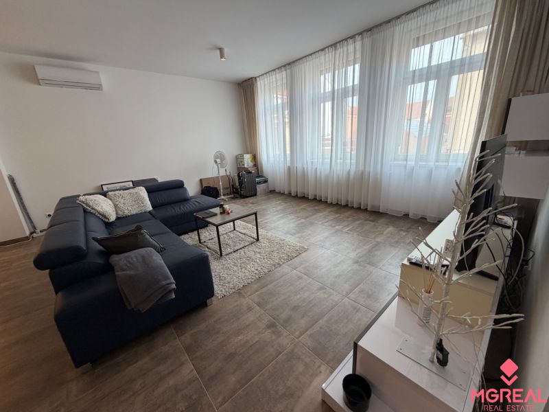 Wohnzimmer in einer 2-Zimmer-Wohnung mit dunklem Sofa und Holzboden.