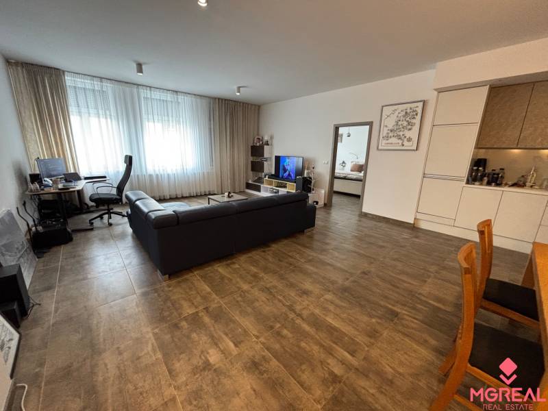 Wohnzimmer einer Zweizimmerwohnung mit dunklem Sofa und Arbeitsecke.