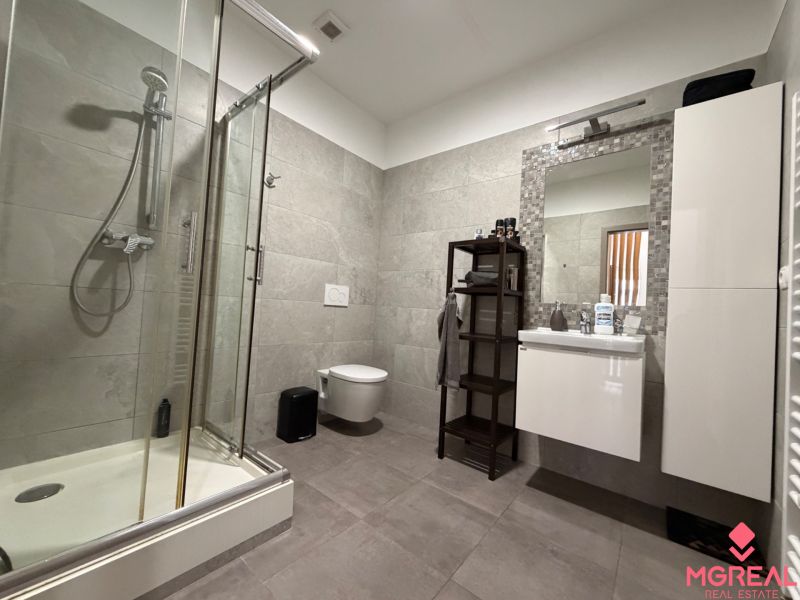 Badezimmer in einer 2-Zimmer-Wohnung mit Duschkabine, Spiegel und stilvollen Fliesen.