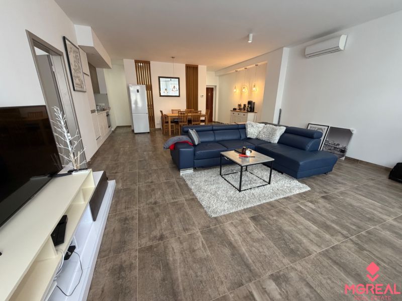 Wohnzimmer mit großem Sofa und Fernseher in einer 2-Zimmer-Wohnung, Boden mit Holzdekor.
