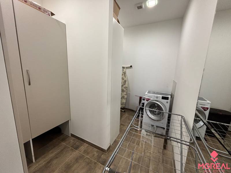 Eine Nische mit Waschmaschine, Trockner und Schrank in einer 2-Zimmer-Wohnung; Boden mit Holzdekor.