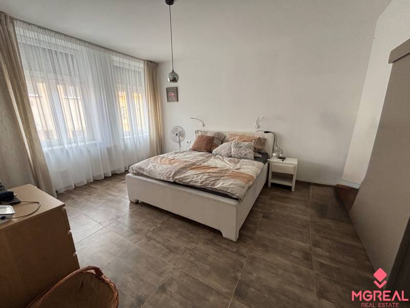 Schlafzimmer in einer 2-Zimmer-Wohnung mit großen Fenstern, einem Bett und einem Boden mit Holzdekor.