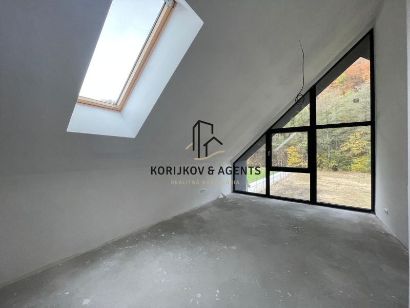 Ein Dachzimmer in einem Einfamilienhaus mit großen Fenstern und Blick auf den Wald.