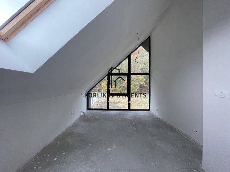 Ein Dachzimmer mit großen Fenstern und einer hervorstehenden Decke in einem Einfamilienhaus, ohne Bodenbelag.