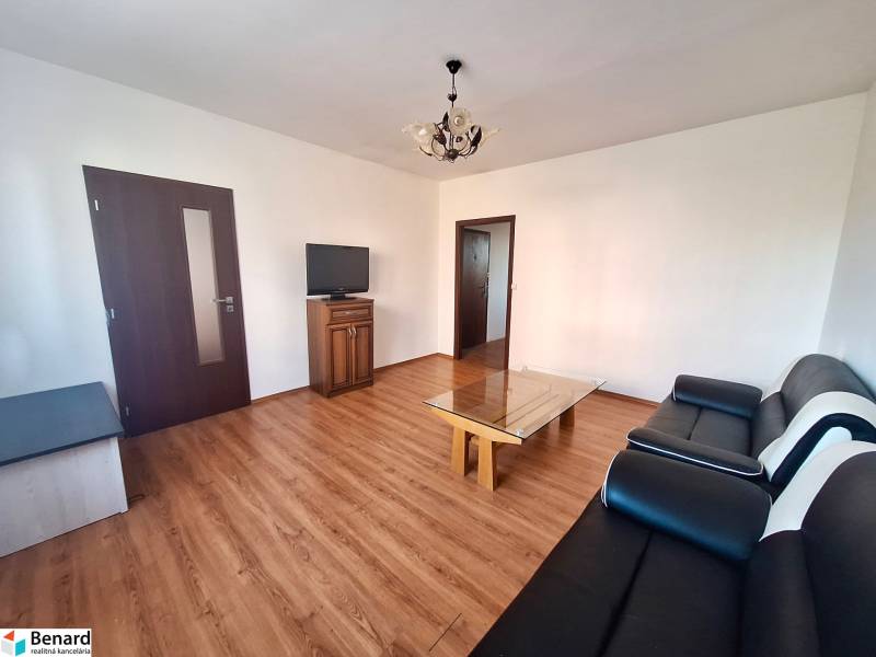 Wohnzimmer in einer 3-Zimmer-Wohnung mit Holzboden, schwarzem Sofa und Fernseher.