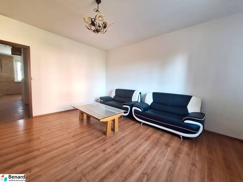 Wohnzimmer in einer 3-Zimmer-Wohnung mit Holzboden und schwarzen Sitzmöbeln.