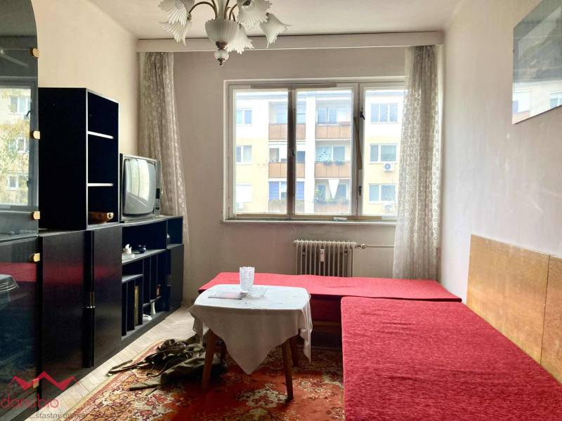 Wohnzimmer in einer 3-Zimmer-Wohnung mit rotem Sofa, Teppich, älterem Fernseher, heller Raum.