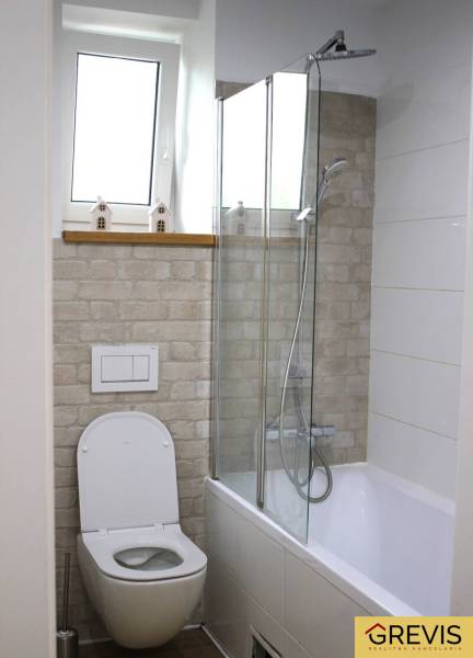 Badezimmer in einer 3-Zimmer-Wohnung mit Badewanne, Dusche, Toilette und dekorativer Wand in Ziegeloptik.