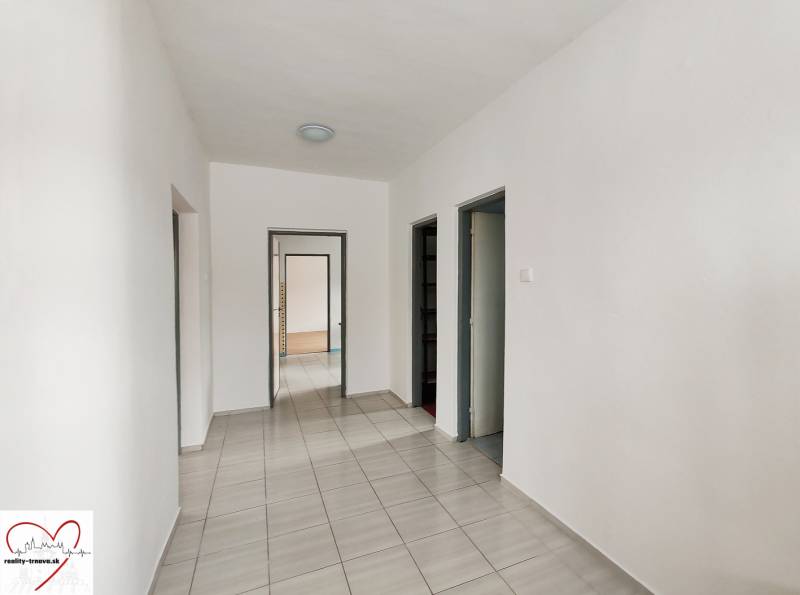 Der Flur des Einfamilienhauses mit Fliesen und weißen Wänden, der zu einer Tür führt.