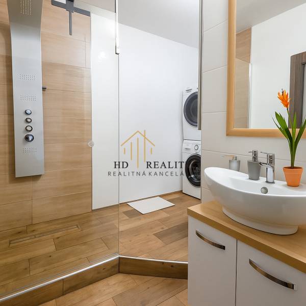 Badezimmer in einer 3-Zimmer-Wohnung mit Waschbecken, Duschkabine und Waschmaschine, mit einem Boden in Holzoptik.