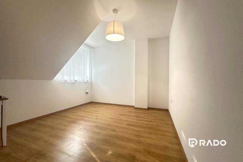 Ein Raum in einem Einfamilienhaus mit einem Holzboden, einer einfachen Lampe und einem großen Fenster.