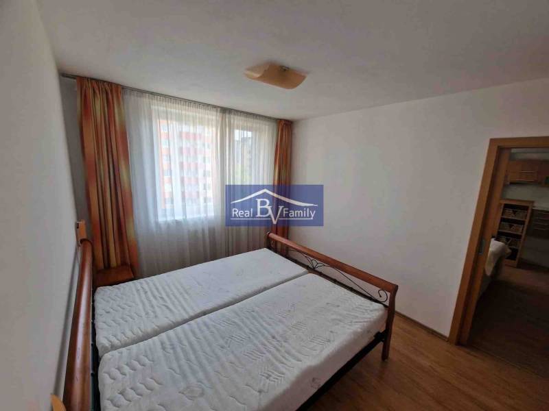 Schlafzimmer in einer 2-Zimmer-Wohnung mit Bett, Vorhängen und Boden in Holzoptik.