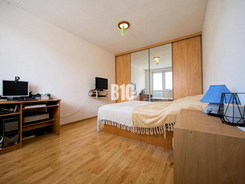 Schlafzimmer in einer 2-Zimmer-Wohnung mit Holzboden, Spiegelschrank und Schreibtisch.