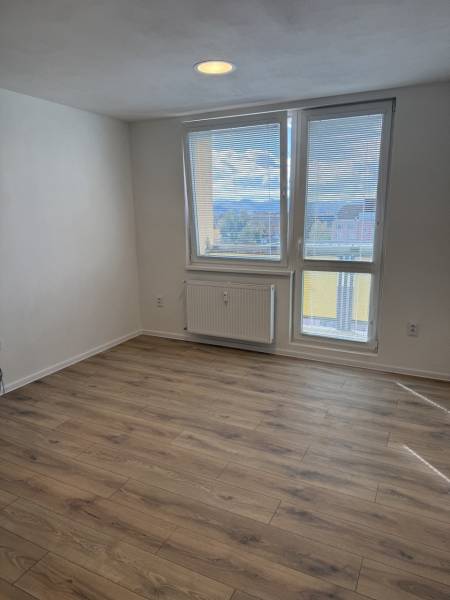 Einzimmerwohnung mit Holzboden und großem Fenster, das einen Ausblick auf die Umgebung bietet.