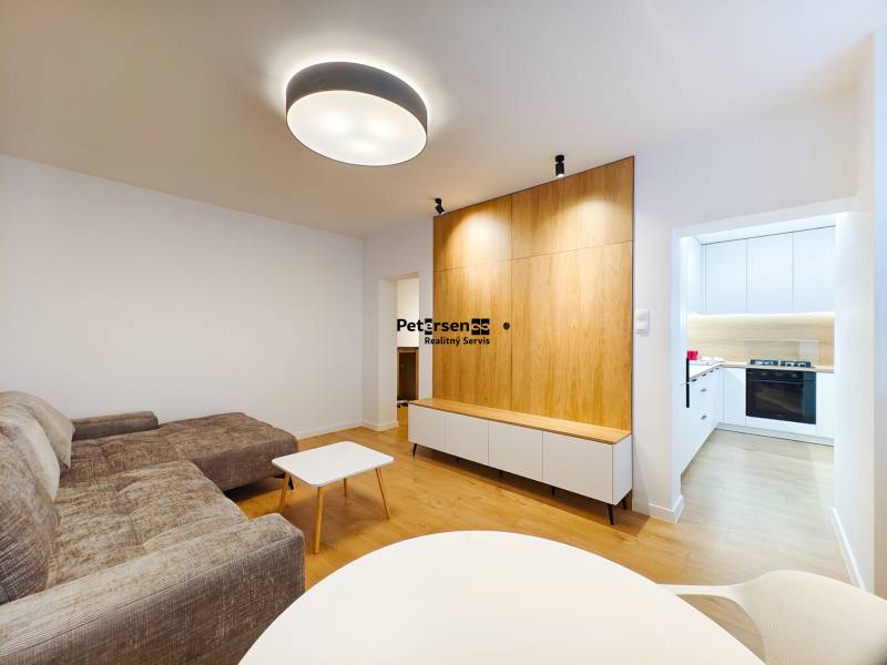 Wohnzimmer in einer Zweizimmerwohnung mit Holzboden und Zugang zur weißen Küche.