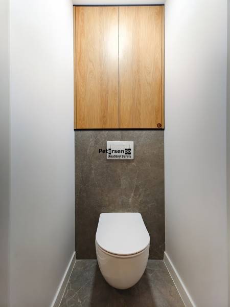 Toilette in einer 2-Zimmer-Wohnung mit dunklem Steinboden und Holzschränken.