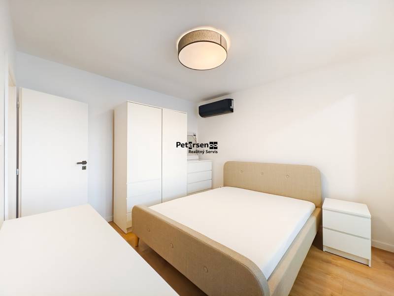 Schlafzimmer in einer 2-Zimmer-Wohnung mit Bett, Schrank, Kommode und Boden in Holzoptik.