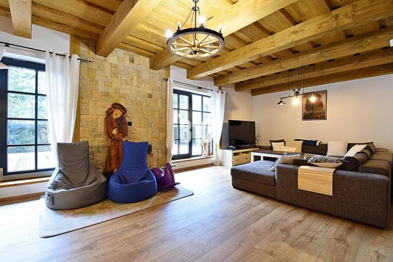 Innenraum einer Hütte mit Steinwand, großem Sofa und Boden in Holzoptik.