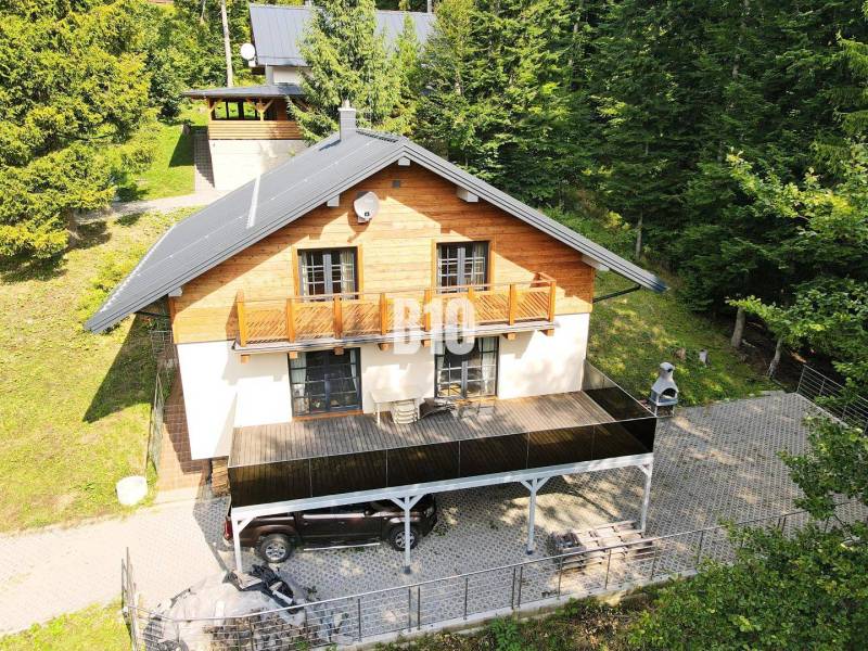 Eine Hütte in Terchová, umgeben von Wald, mit Terrasse, Auto, Grill und Holzelementen.