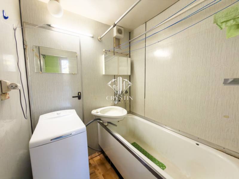 Badezimmer in einer 3-Zimmer-Wohnung mit Badewanne, Waschbecken und Waschmaschine, Boden mit Holzdekor.