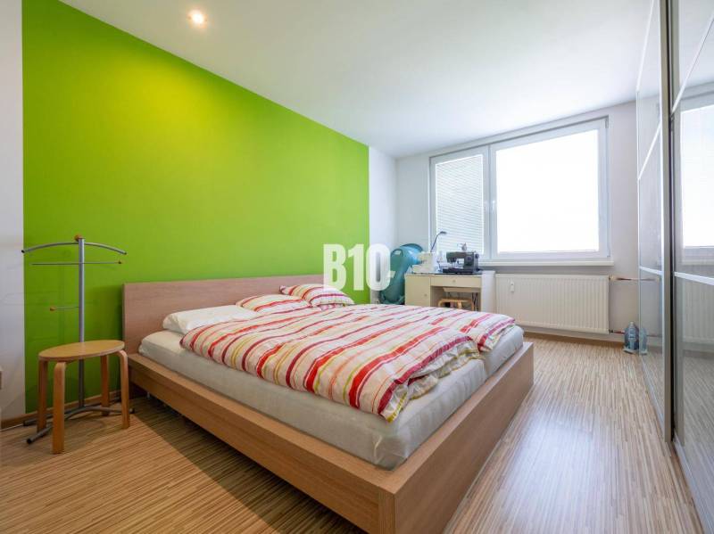 Schlafzimmer in einer 4-Zimmer-Wohnung mit Holzboden und grüner Wand.