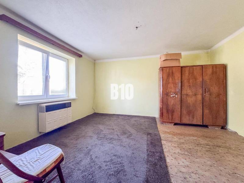 Ein Zimmer in einem Einfamilienhaus mit Teppich, einem alten Schrank und einem Sessel.