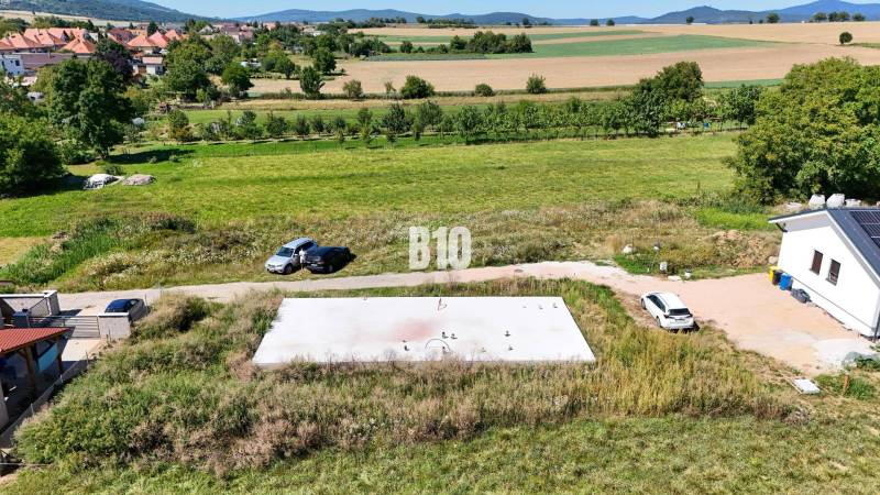 Grundstücke - Wohnen in Čeľadice mit Häusern, Autos und natürlicher Landschaft im Hintergrund.