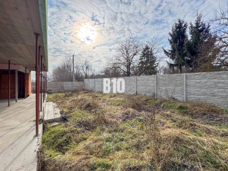 Der Bau eines Einfamilienhauses mit einem Rasenstück und einem Zaun, unter einem bewölkten Himmel.