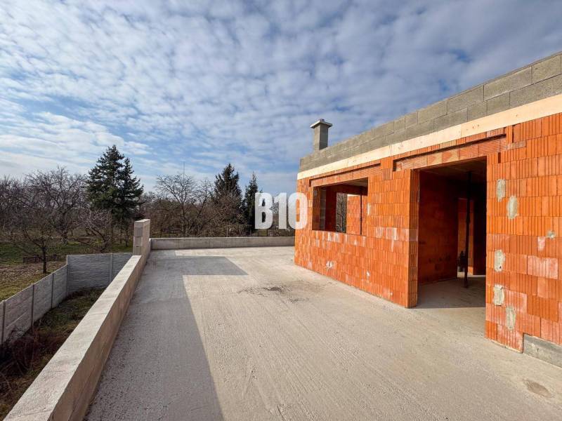 Ein im Bau befindliches Einfamilienhaus mit Terrasse auf einem großen Hof, umgeben von Natur und Bäumen.