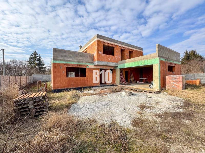 Unvollendeter Ziegel-Einfamilienhausbau, umgeben von Gras und Holzpaletten.