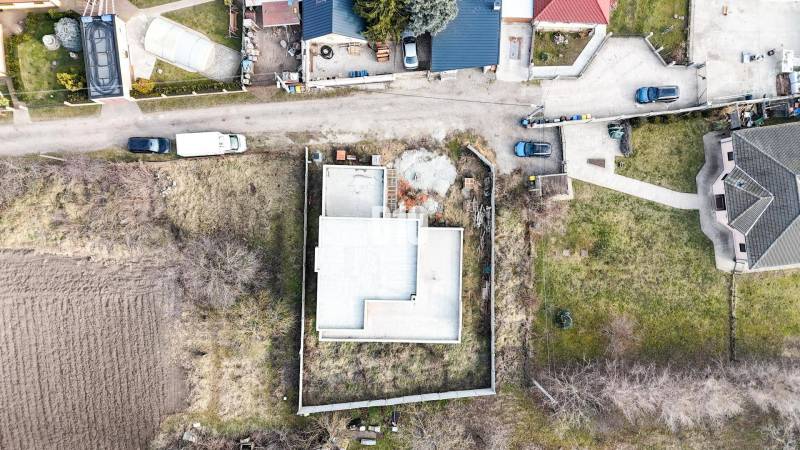Ein im Bau befindliches Einfamilienhaus auf einem Grundstück, umgeben von einem Garten und benachbarten Häusern.