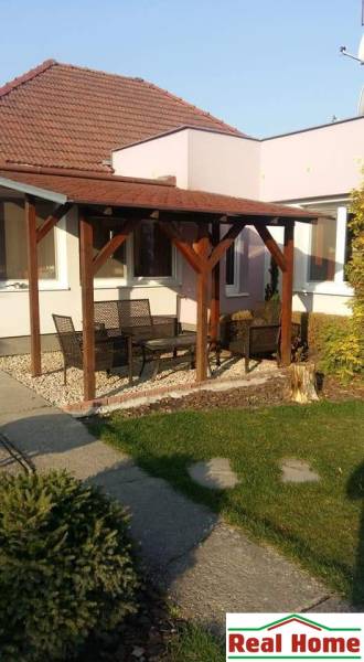 Ein Einfamilienhaus in Čierna Voda mit Terrasse, Gartenmöbeln und grünem Rasen.