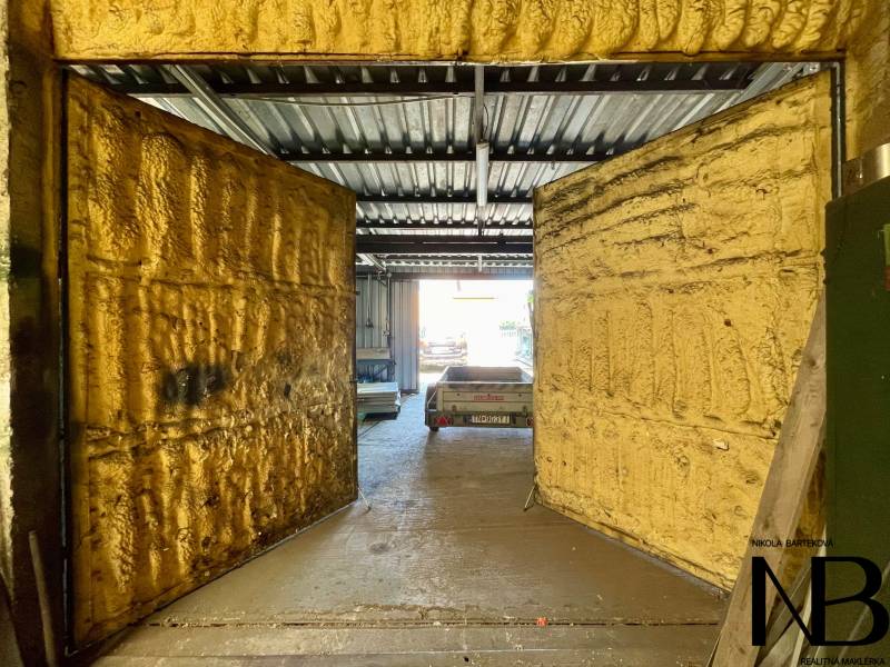 Geschäftsräume mit offenen Türen und einem Metalldach, im Hintergrund ist ein Auto zu sehen.