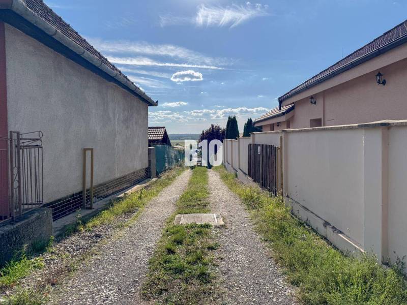Ein schmaler Weg zwischen den Häusern im Gebiet Pozemky - Wohnen, Nitra, der zu einem Panoramablick auf die Landschaft führt.