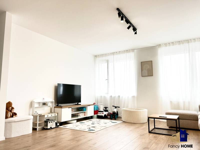 Wohnzimmer in einer 2-Zimmer-Wohnung mit Fernseher, Spielzeug und Boden in Holzoptik.