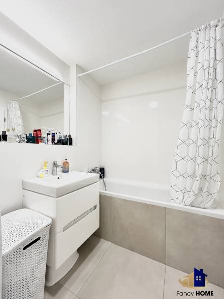 Badezimmer mit Badewanne und Vorhang in einer 2-Zimmer-Wohnung, weißer Schrank und Wäschekorb.