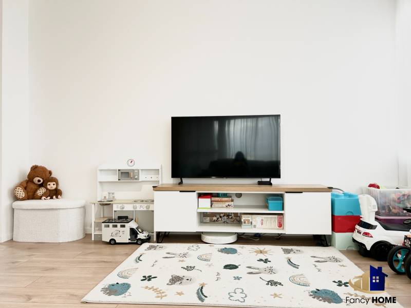 Wohnzimmer in einer 2-Zimmer-Wohnung mit Spielzeug, Fernseher und Boden in Holzoptik.