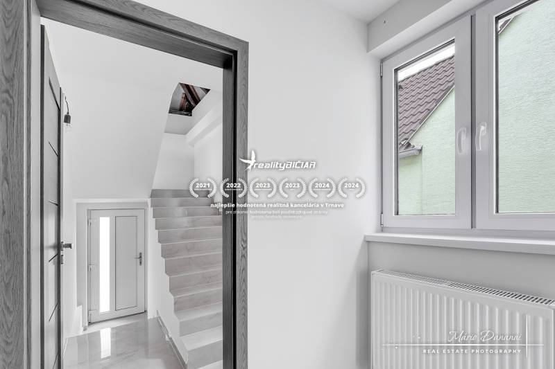 Innenraum eines Einfamilienhauses mit weißen Wänden, Treppe und großem Fenster.