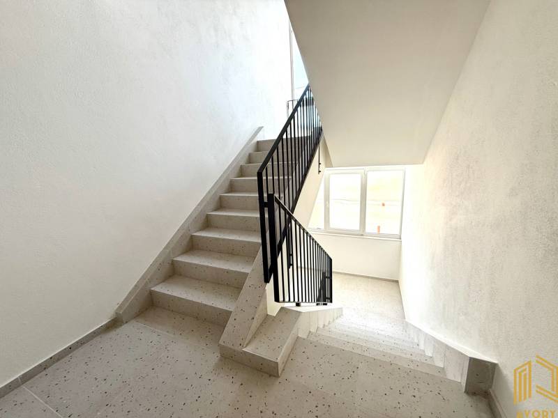 Treppenhaus in einem Wohnhaus mit Fenster, weiße Wände und Fliesen.