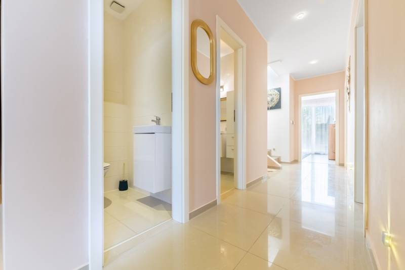 Der Flur im Einfamilienhaus mit hellen Fliesen, offene Tür zum Badezimmer, Spiegel an der Wand.