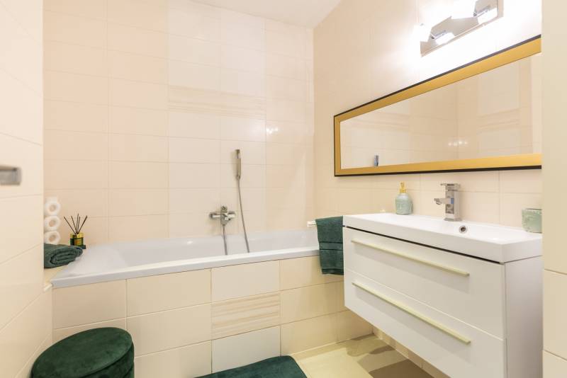 Badezimmer mit Spiegel, Badewanne und Waschbecken in einem Einfamilienhaus, helle Fliesen.